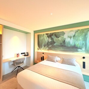Habitación de hotel con una cama grande, un escritorio con silla y un mural grande en la pared.