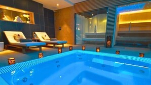 Moderni spa-alue, jossa on poreallas, kaksi aurinkotuolia ja lasiseinällinen sauna.