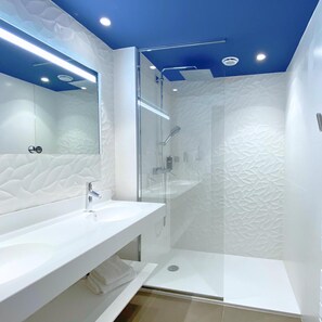 Un baño moderno con tocador blanco, cabina de ducha con vidrio y techo con detalles azules.