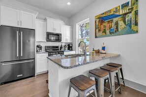 A modern kitchen with white cabinets, stainless steel appliances, a granite countertop, and a painting of a street scene. - Sand Star Oasis near beaches of 30A (Santa Rosa Beach)