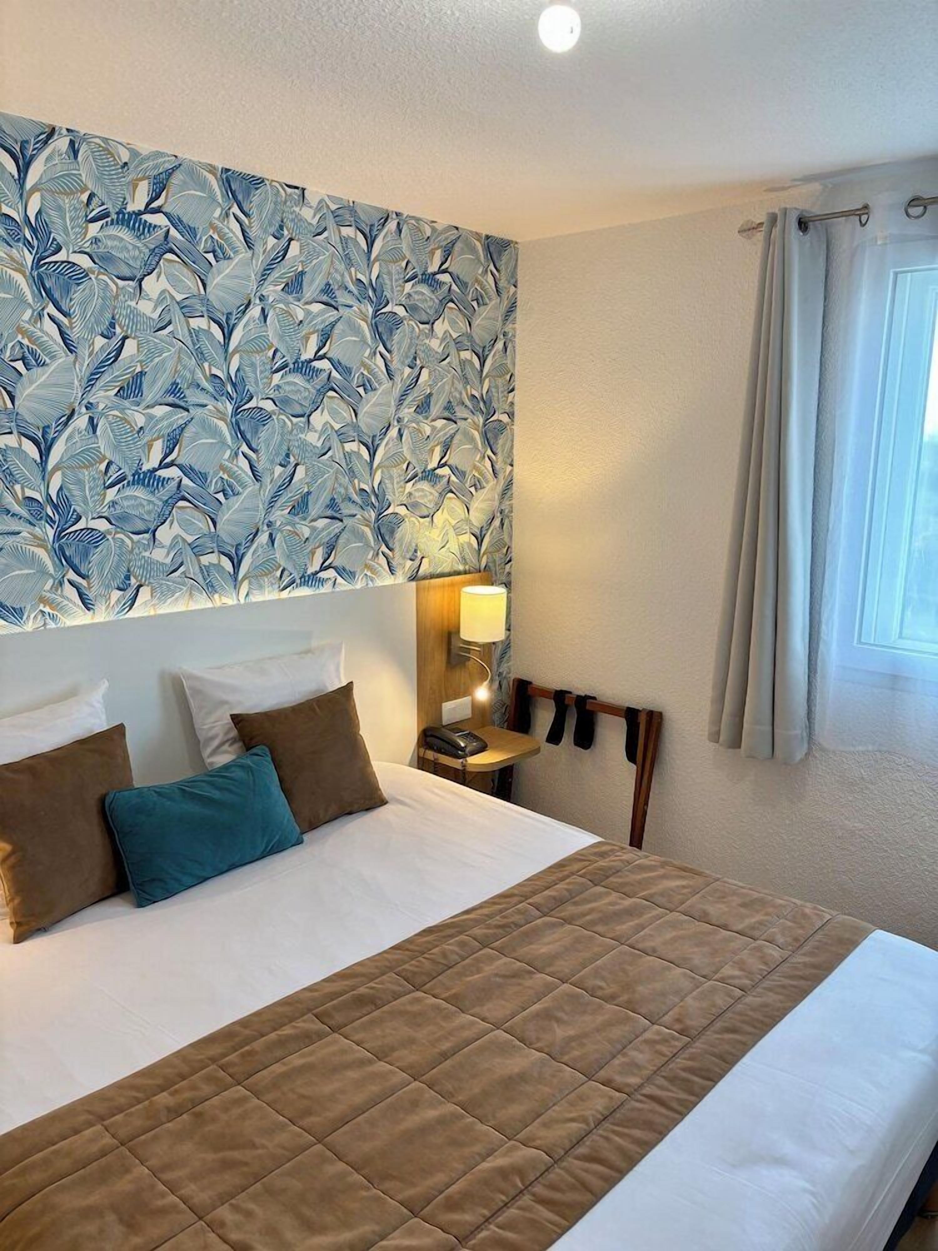 A hotel room with a large bed, a nightstand with a lamp, and a window with curtains.