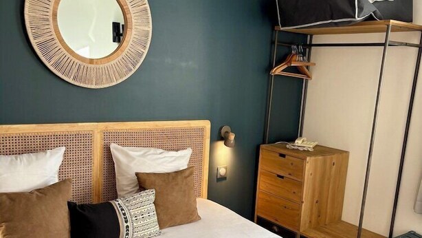Une chambre d’hôtel avec un lit, un miroir rond, une armoire et un porte-manteau.
