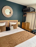 Una habitación de hotel con cama, espejo redondo, armario y perchero.