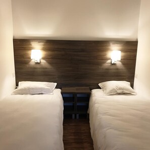 A hotel room with two beds, each with white bedding and pillows. There are wall-mounted lights above the beds. - Hotel Des Portes De Meuse (Pagny-sur-Meuse)