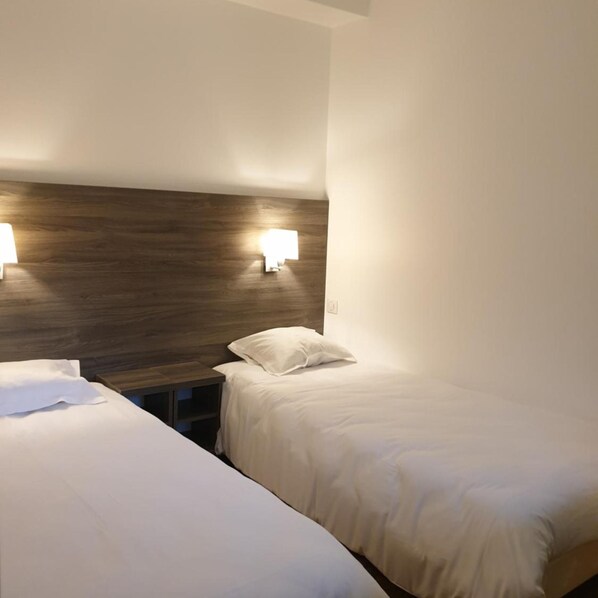 A hotel room with two single beds, a wooden headboard, and wall-mounted reading lamps. - Hotel Des Portes De Meuse (Pagny-sur-Meuse)