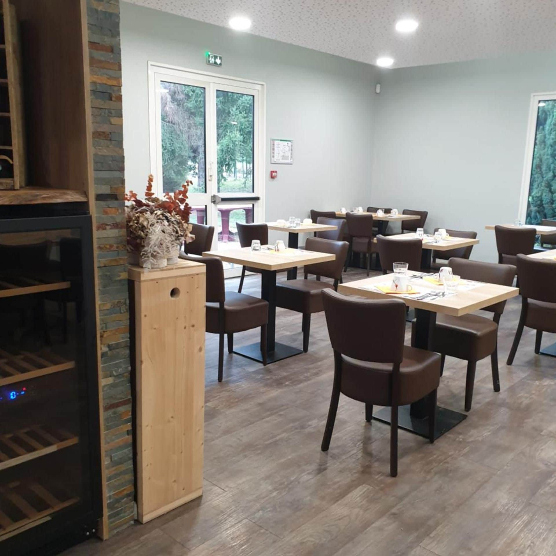 Comedor con varias mesas y sillas, una encimera de madera y vistas al exterior a través de amplios ventanales.