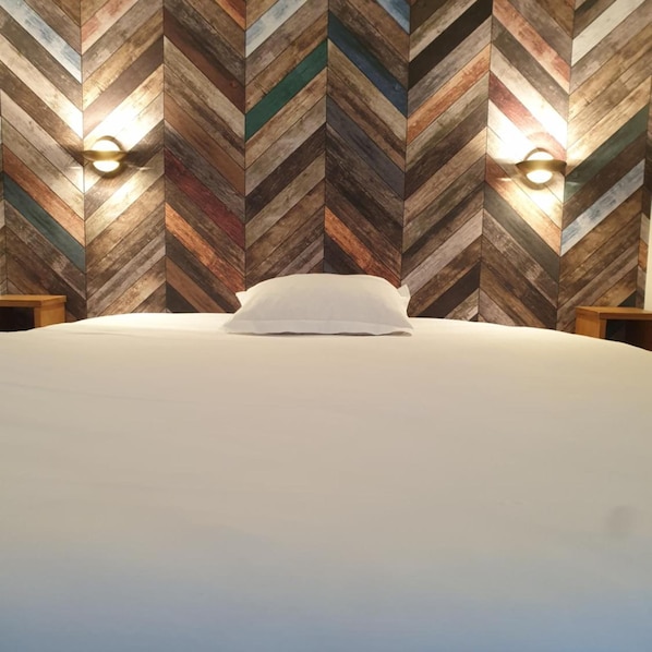 Una cama con sábana blanca en una habitación con pared de madera con diseño de espiga.