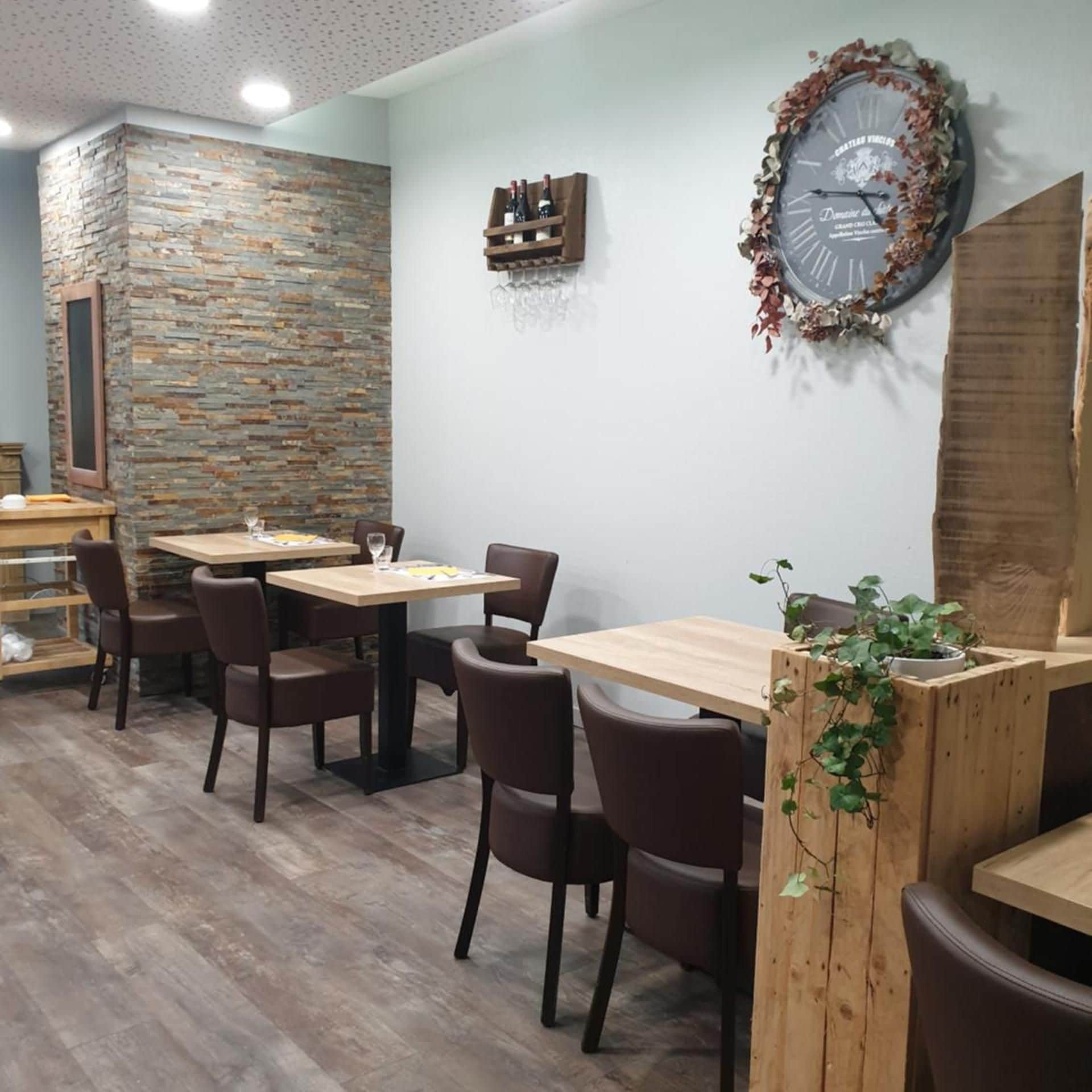 A restaurant interior with wooden tables and chairs, a stone accent wall, a clock, and a small plant.