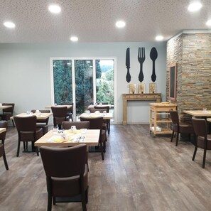 Un comedor con mesas y sillas, un muro de piedra y vistas al exterior con vegetación.