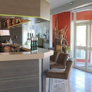 A modern bar area with a counter, bar stools, and a decorative plant arrangement. - Hotel Des Portes De Meuse (Pagny-sur-Meuse)