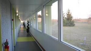 A corridor with windows, a fire extinguisher, and a view of a grassy area. - Hotel Des Portes De Meuse (Pagny-sur-Meuse)
