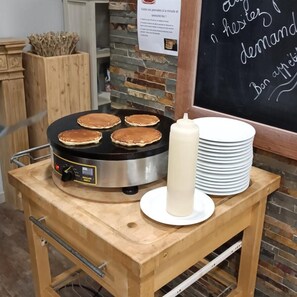 A breakfast setup with pancakes on a griddle, a stack of white plates, and a bottle of syrup. - Hotel Des Portes De Meuse (Pagny-sur-Meuse)