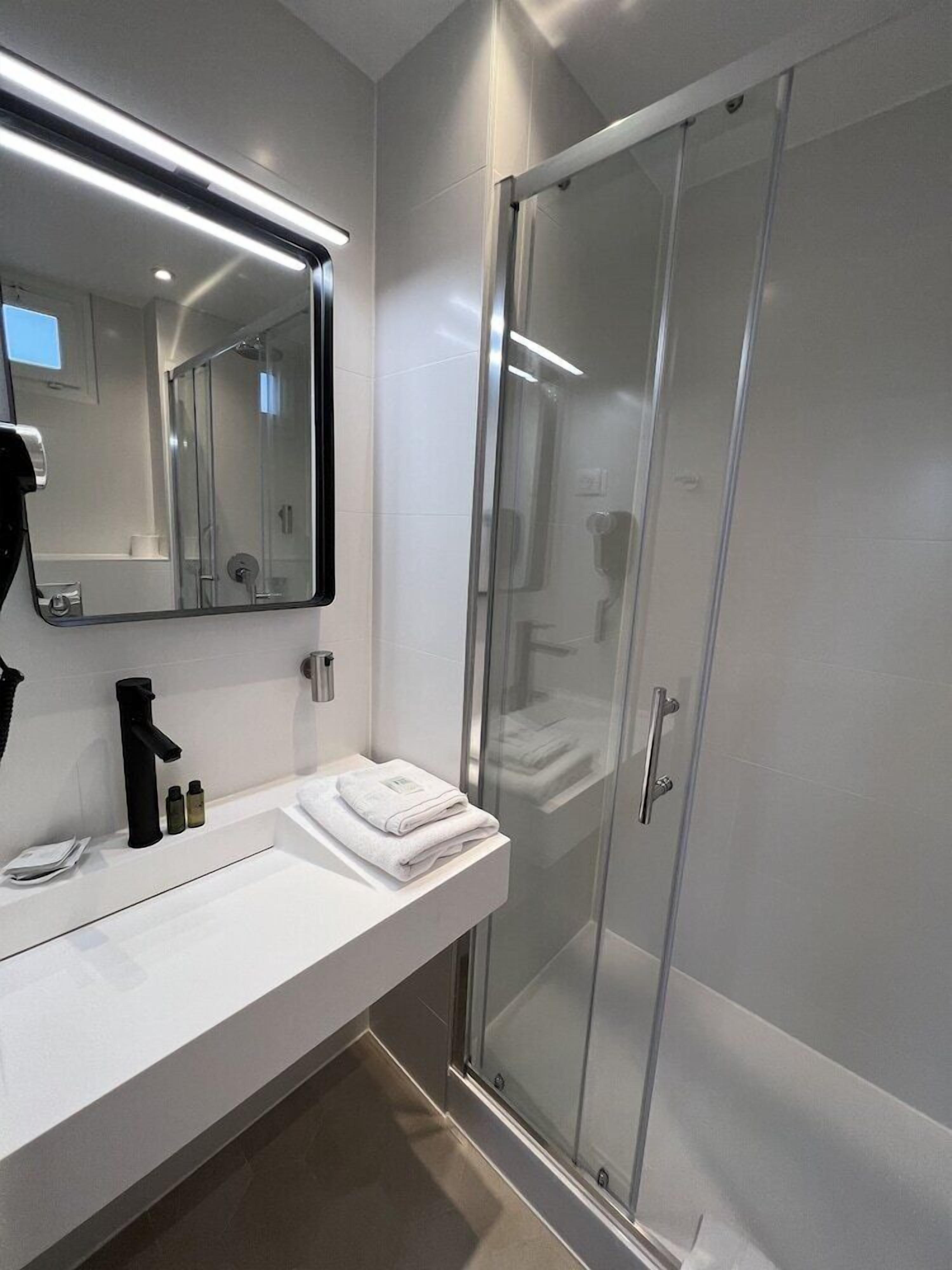 Une salle de bain moderne avec une douche à parois de verre, un lavabo blanc avec un miroir au-dessus et un porte-serviettes.