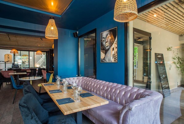 A modern restaurant interior with a blue wall, a wooden table set with wine glasses, and a cushioned bench. - Paris (Saint-Cloud)
