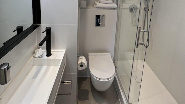 A modern bathroom with a glass shower enclosure, a white toilet, and a vanity with a mirror and towel rack.