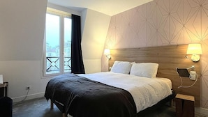 A hotel room with a bed, bedside lamps, a window with curtains, and a geometric-patterned wall.