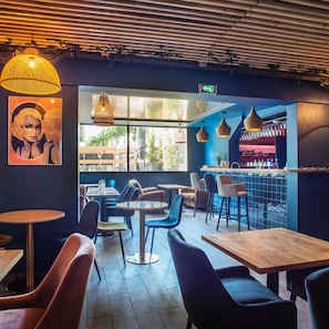 Interior de restaurante com mesas, cadeiras, luminárias pendentes e um espaço de bar.