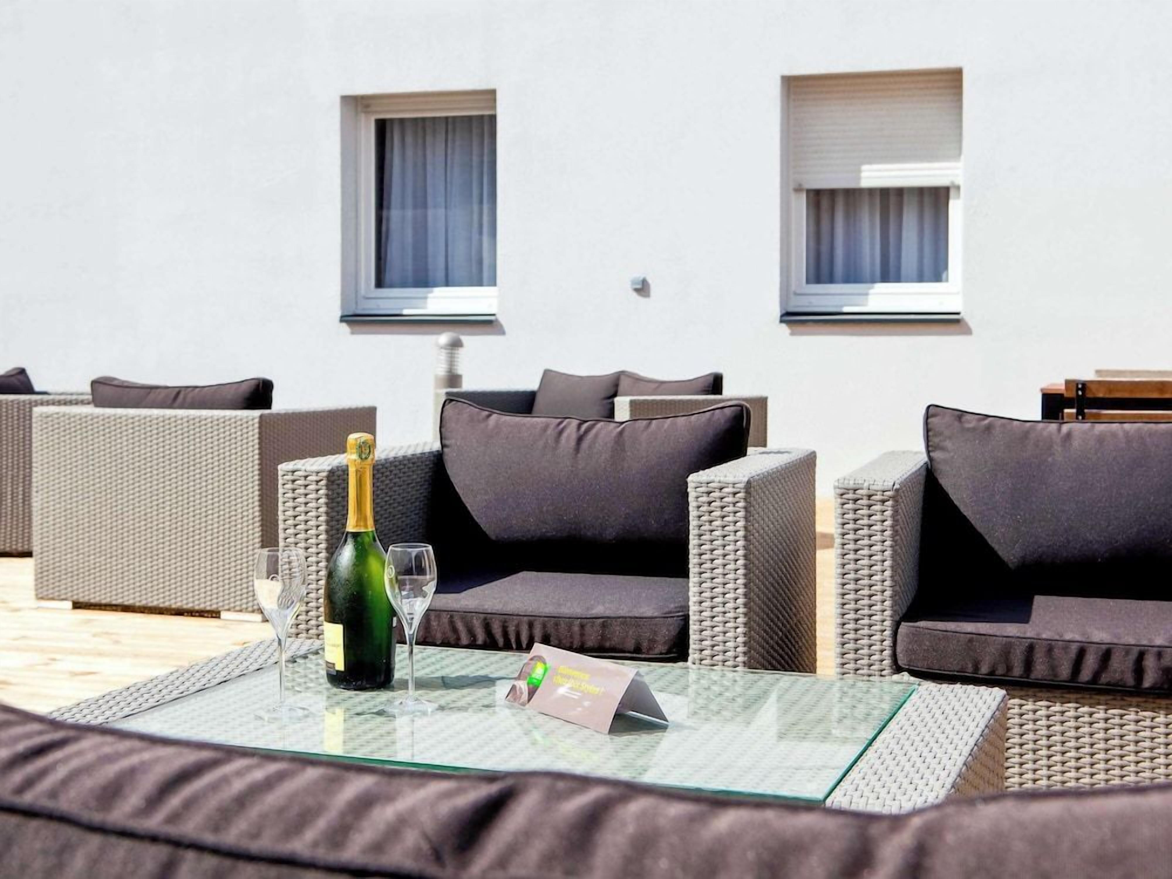 Ein sonnendurchfluteter Außenbereich mit Korbmöbeln und einem Glastisch, mit einer Champagnerflasche und einem Glas.
