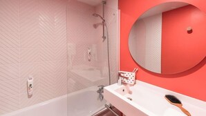 A bathroom with a white bathtub, a shower, a sink with a mirror, and a toothbrush holder. - Ibis Styles Chlons-en-champagne Centre (Chalons-en-Champagne)