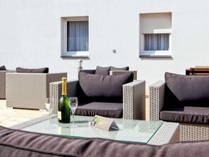 A sunlit outdoor seating area with wicker furniture and a glass table, featuring a bottle of champagne and a glass. - Ibis Styles Chlons-en-champagne Centre (Chalons-en-Champagne)