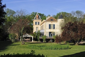 Un grand bâtiment historique doté d’une tour et de nombreuses fenêtres, entouré de jardins et d’arbres bien entretenus.