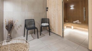 A modern spa room with two black chairs, a wooden bench, and a glass door leading to a sauna. - Hotel Tignes Le Diva (Tignes)