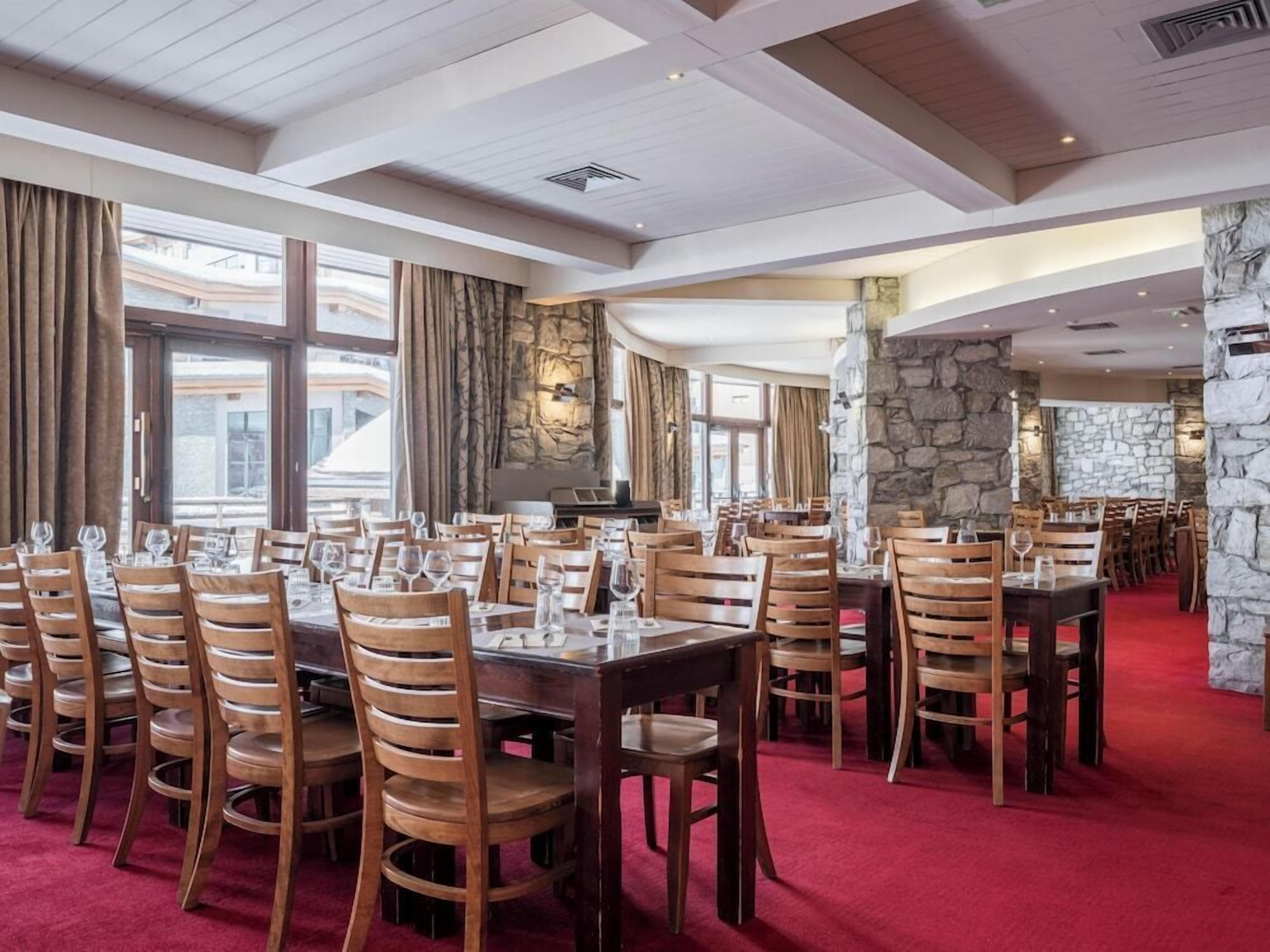 A restaurant with multiple tables and chairs, stone walls, and large windows.