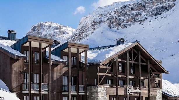 A multi-story lodge with a stone facade, wooden balconies, and a mountainous backdrop. - Hotel Tignes Le Diva (Tignes)