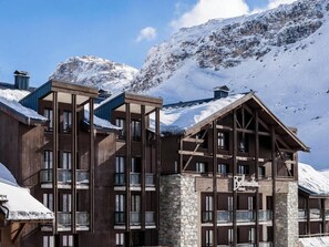 A multi-story lodge with a stone facade, wooden balconies, and a mountainous backdrop. - Hotel Tignes Le Diva (Tignes)