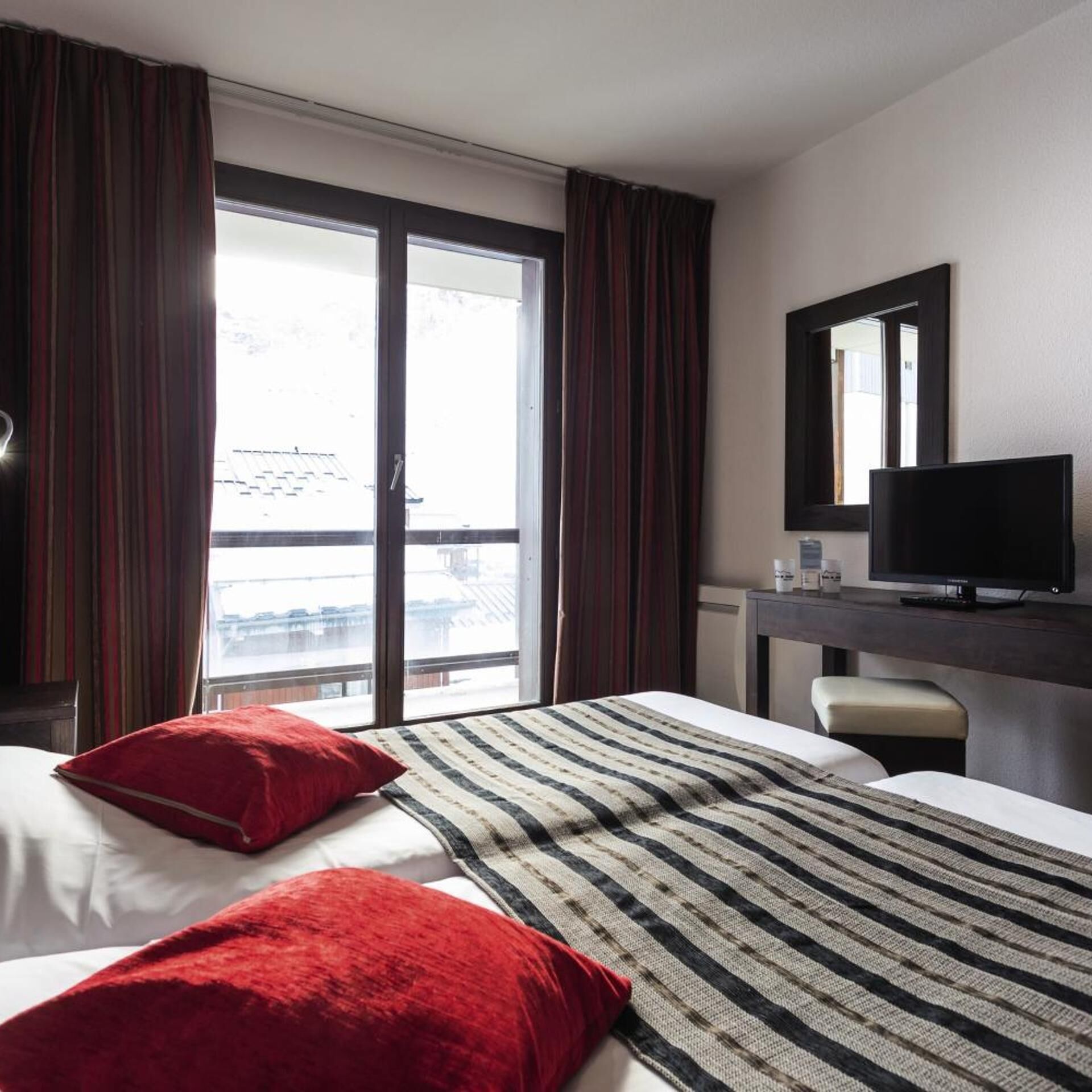 Een hotelkamer met een bed, een bureau met televisie, een raam met gordijnen en uitzicht op buiten.
