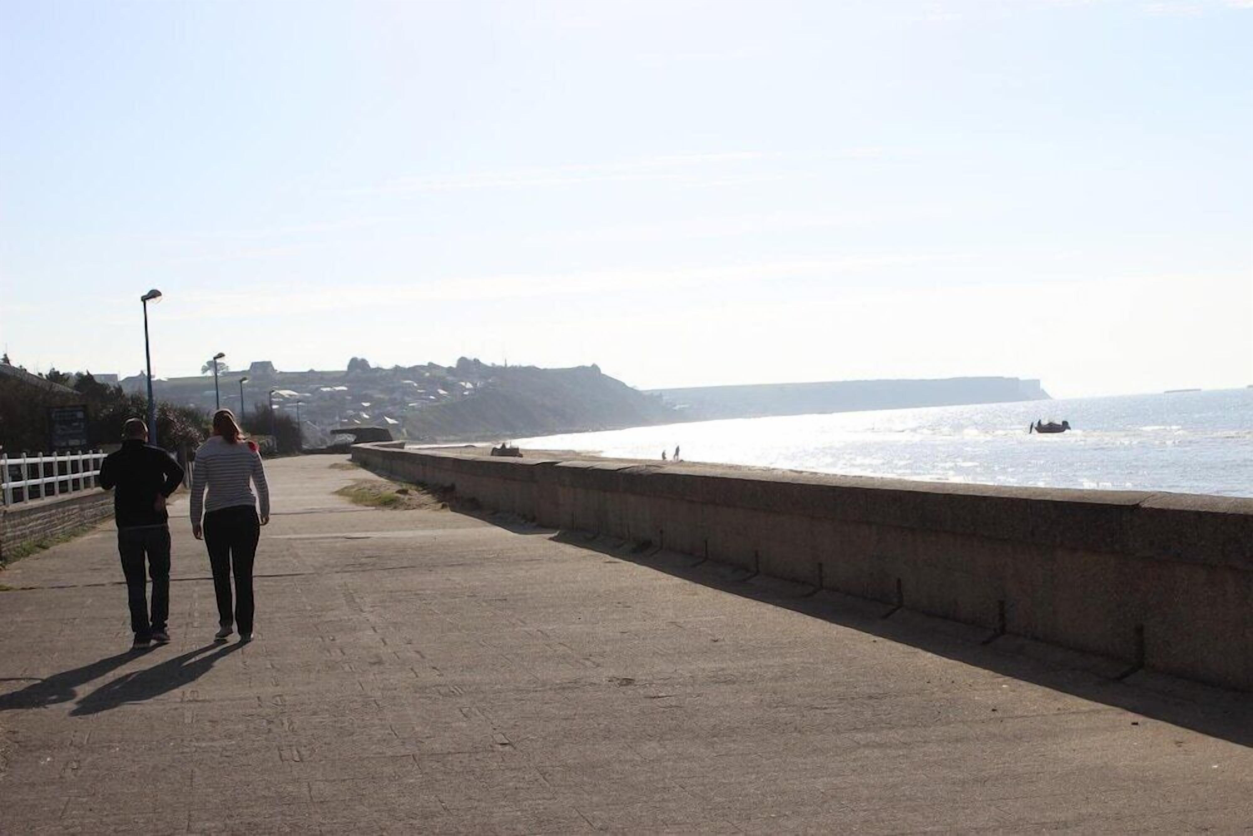 A concrete pathway beside a body of water with a distant view of a town.