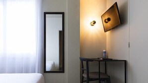 Ein Hotelzimmer mit einem Bett, einem Schreibtisch mit Stuhl, einem Wand-Fernseher und einem Spiegel.