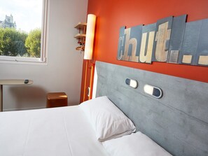 Habitación de hotel con cama, mesita de noche, lámpara y vistas a un castillo por la ventana.