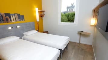 A hotel room with two beds, a window with a view of a building, a TV, and a small table.