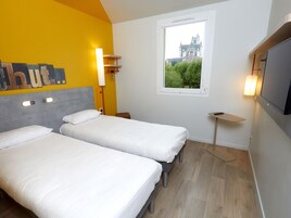 A hotel room with two beds, a window with a view of a building, a TV, and a small table.