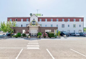 A B&B hotel with a central entrance, parking lot, and a row of windows on the building facade. - B&B Hôtel Lyon Saint-bonnet Mi-plaine (Saint-Bonnet-de-Mure)