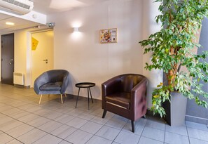 Een moderne lobby met een bruine leren fauteuil, een klein rond tafeltje en een potplant.