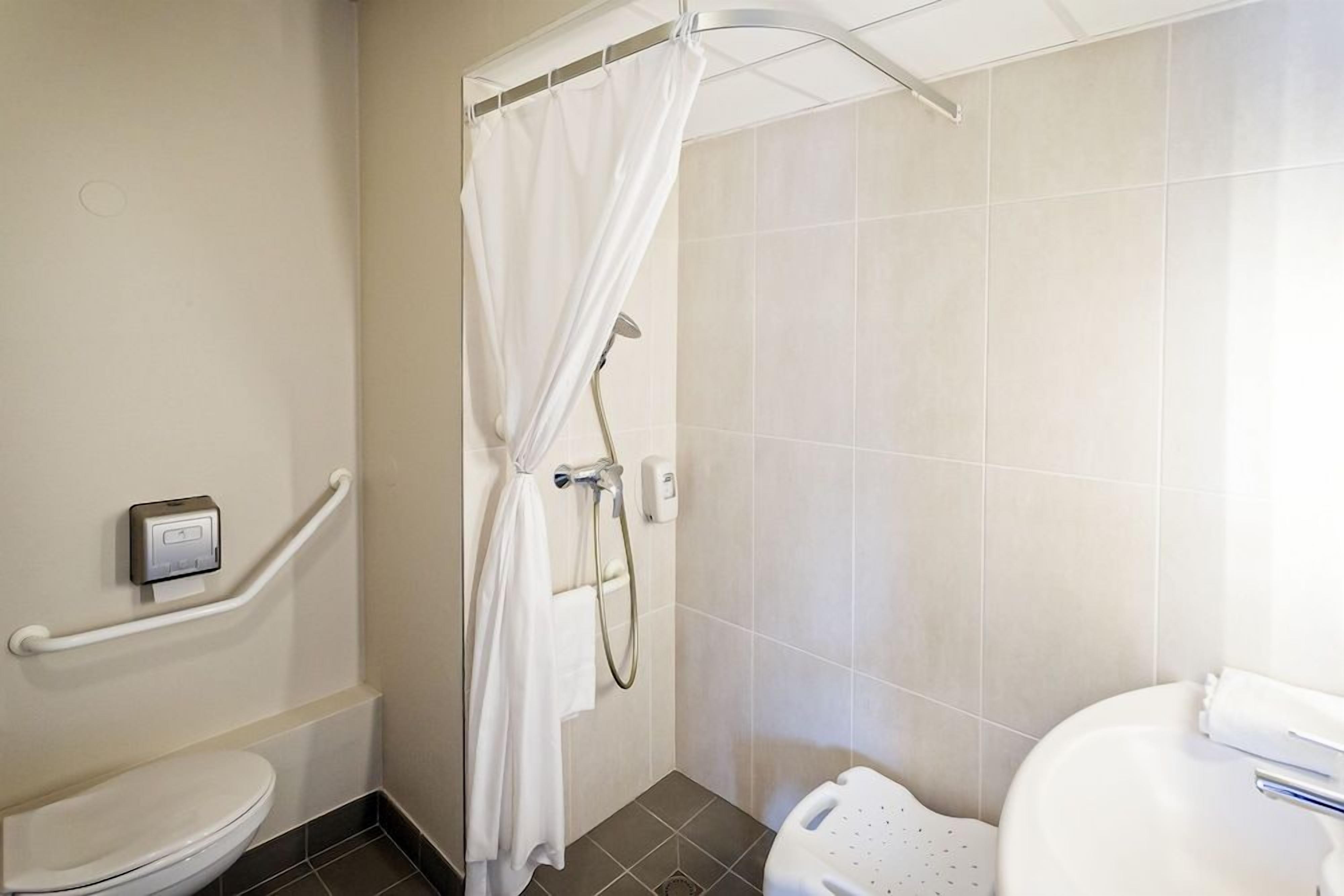 A bathroom with a shower, toilet, and handrails.