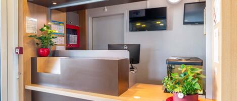 A reception desk with a computer, a potted plant, and a wall-mounted TV.