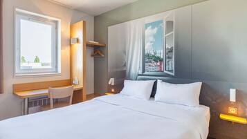 Ein Hotelzimmer mit einem großen Bett, einem Schreibtisch, einem Sessel und einem Fenster mit Blick auf die Stadt.