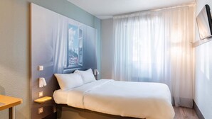 A hotel room with a bed, bedside tables, a mounted TV, and a window with curtains.