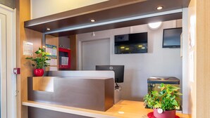 A reception desk with a computer, a potted plant, and a wall-mounted TV.