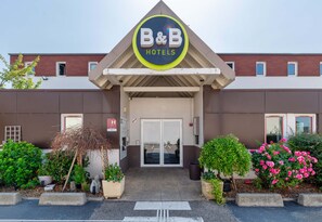 The exterior of B&B Hotels with a prominent sign, a covered entrance, and well-maintained landscaping. - B&B Hôtel Lyon Saint-bonnet Mi-plaine (Saint-Bonnet-de-Mure)