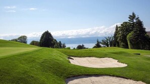A golf course with a sand bunker, green hills, and a lake in the background. - Minotel Le Bourgogne (Evian-les-Bains)
