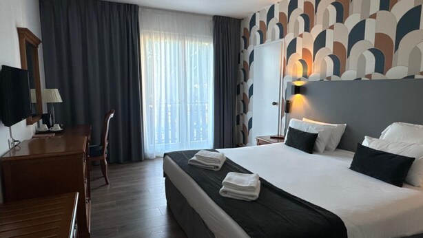 A hotel room with a large bed, a desk, a chair, and a window with curtains. - Minotel Le Bourgogne (Evian-les-Bains)