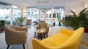 A hotel lobby with seating, a table with a bottle and glasses, and large windows. - Minotel Le Bourgogne (Evian-les-Bains)