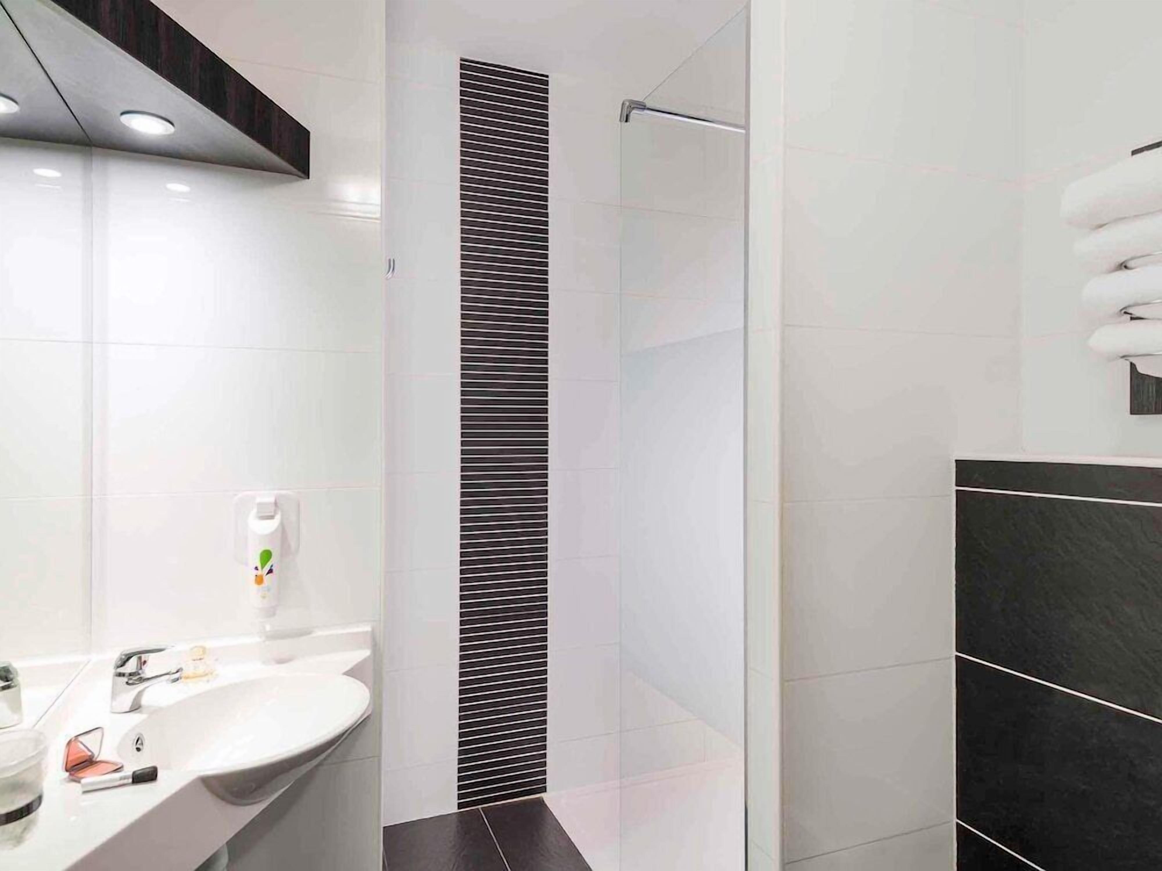 A modern bathroom with a white sink, a mirror, a towel rack, and a shower area.
