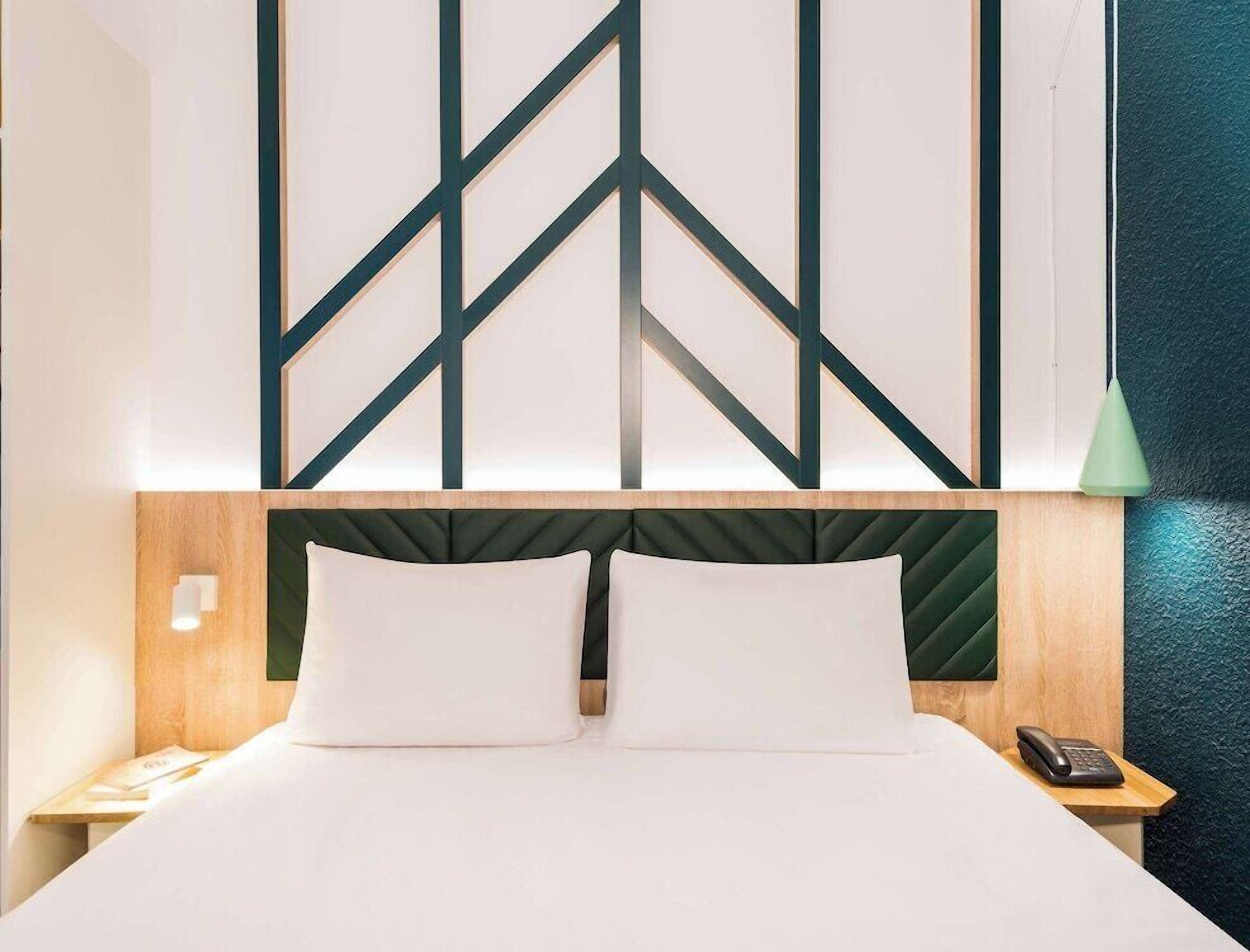 A hotel room with a bed, a nightstand, a telephone, and a wall with geometric patterns.
