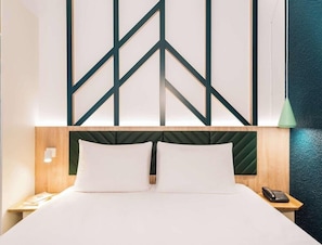 Una habitación de hotel con una cama, una mesita de noche, un teléfono y una pared con diseños geométricos.