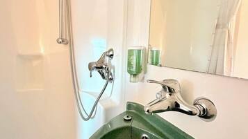 Une salle de bain avec un lavabo vert, une douchette à main, un miroir et un porte-serviettes.